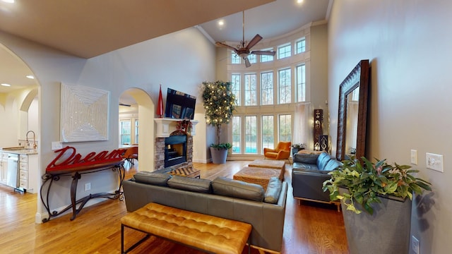 living room with a stone fireplace, ceiling fan, a towering ceiling, and a healthy amount of sunlight