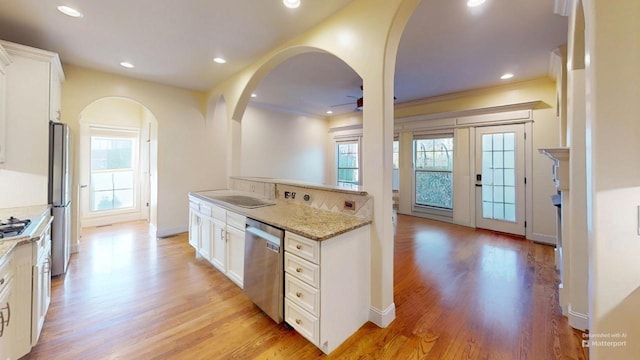 kitchen with appliances with stainless steel finishes, light wood-type flooring, white cabinetry, and light stone counters