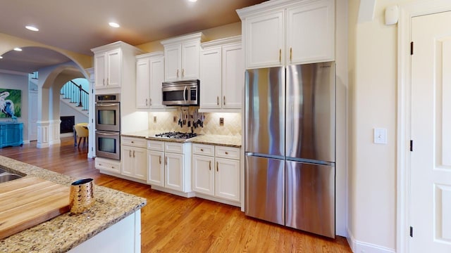 kitchen with backsplash, light stone counters, stainless steel appliances, white cabinets, and light hardwood / wood-style floors