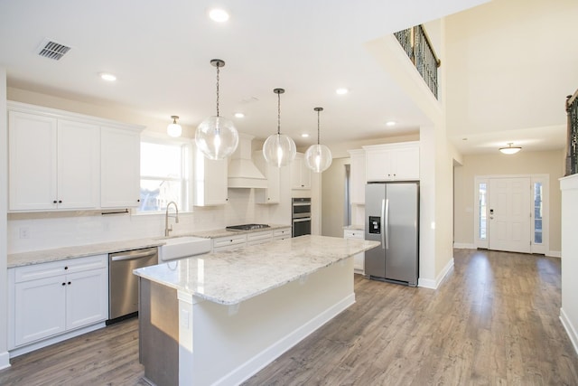 kitchen with appliances with stainless steel finishes, white cabinets, hardwood / wood-style floors, a kitchen island, and hanging light fixtures