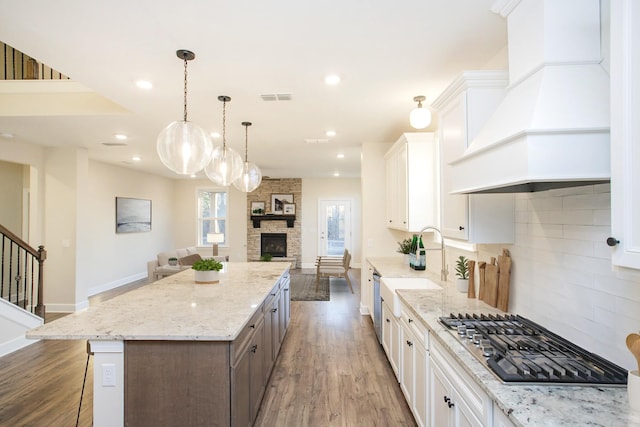 kitchen featuring premium range hood, gas stovetop, a spacious island, a fireplace, and white cabinetry