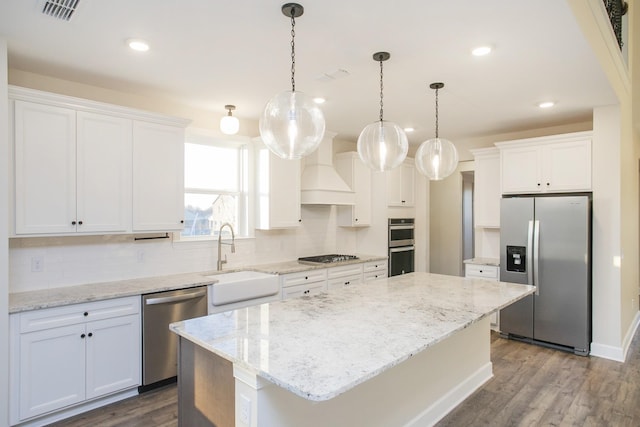 kitchen with a center island, sink, custom range hood, appliances with stainless steel finishes, and white cabinetry