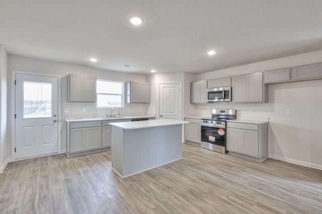 kitchen featuring stainless steel appliances, sink, light hardwood / wood-style flooring, gray cabinets, and a kitchen island