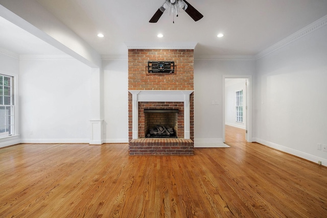 unfurnished living room with hardwood / wood-style flooring, ceiling fan, crown molding, and a brick fireplace