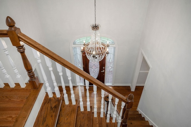 staircase featuring wood-type flooring, a towering ceiling, and a notable chandelier