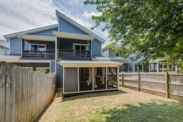 rear view of property with a yard, a balcony, and a sunroom