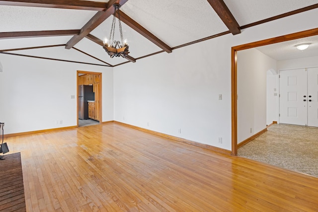 unfurnished living room featuring a chandelier, vaulted ceiling with beams, a textured ceiling, and light hardwood / wood-style floors