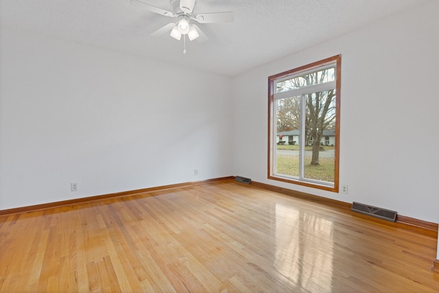 unfurnished room featuring plenty of natural light, ceiling fan, light wood-type flooring, and a textured ceiling