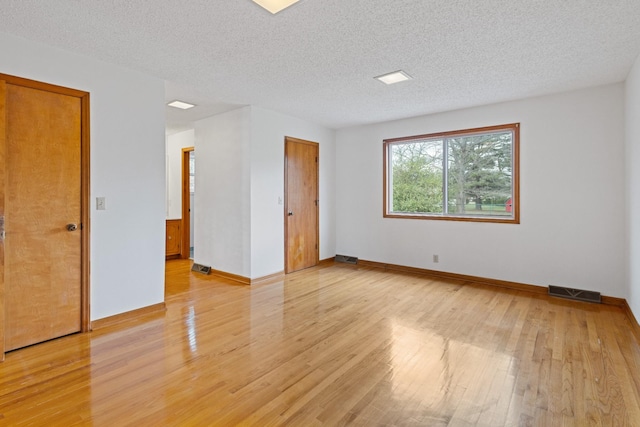 empty room with a textured ceiling and light hardwood / wood-style floors