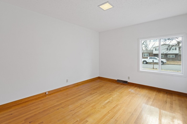 empty room with a textured ceiling and light hardwood / wood-style floors