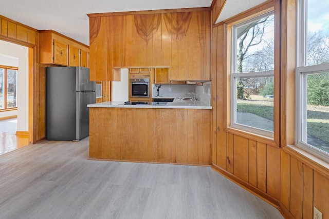 kitchen with kitchen peninsula, appliances with stainless steel finishes, light hardwood / wood-style flooring, and a healthy amount of sunlight