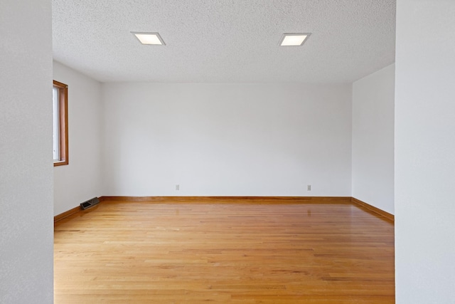 empty room with a textured ceiling and light hardwood / wood-style flooring