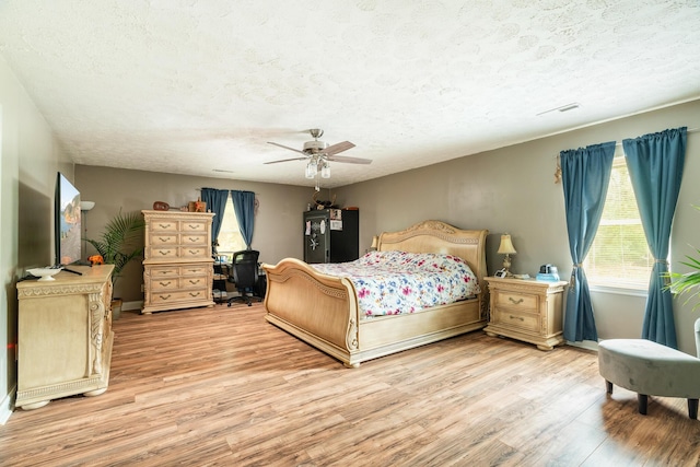 bedroom with ceiling fan, a textured ceiling, and light hardwood / wood-style flooring