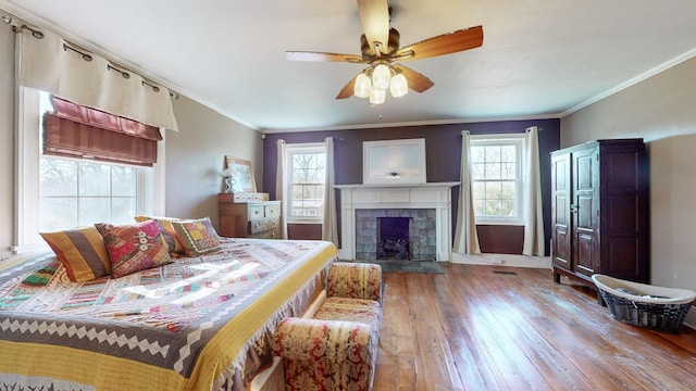 bedroom with a tile fireplace, ceiling fan, hardwood / wood-style floors, and crown molding