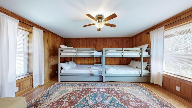 bedroom with multiple windows, ceiling fan, wooden walls, and light hardwood / wood-style floors