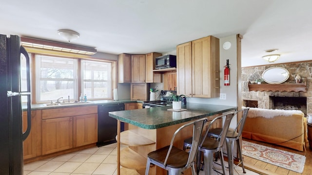 kitchen with black appliances, a kitchen breakfast bar, a stone fireplace, sink, and light tile patterned flooring