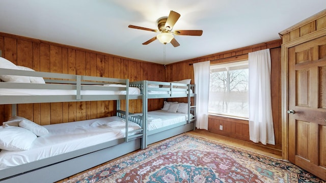 bedroom featuring ceiling fan, hardwood / wood-style floors, and wood walls