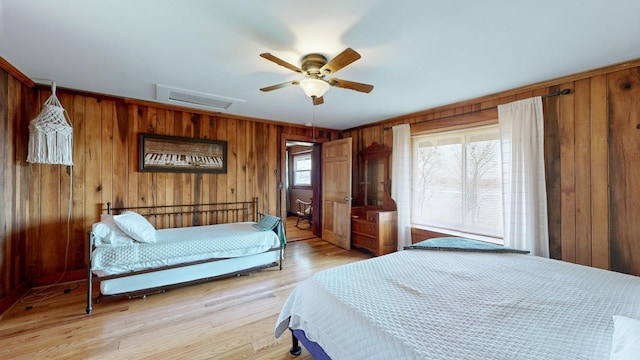 bedroom with ceiling fan, wooden walls, and light wood-type flooring