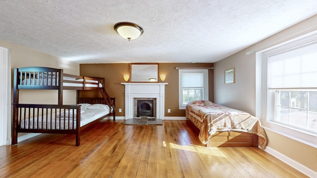 bedroom with a tiled fireplace, hardwood / wood-style floors, and a textured ceiling