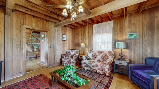 living room featuring wooden walls, hardwood / wood-style floors, beamed ceiling, and ceiling fan