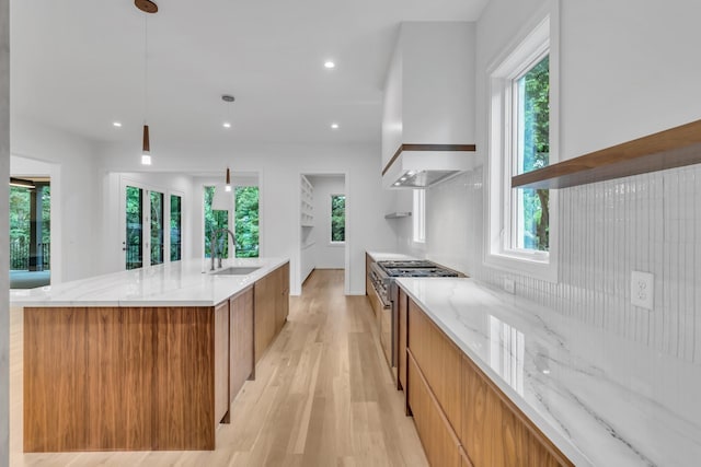 kitchen featuring a spacious island, sink, stainless steel stove, decorative light fixtures, and custom range hood