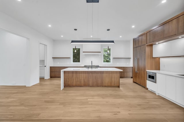 kitchen featuring decorative light fixtures, light hardwood / wood-style flooring, white cabinetry, and a kitchen island with sink