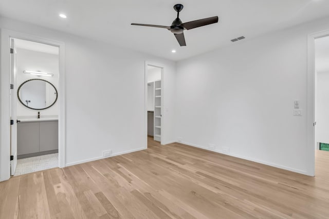 interior space featuring ensuite bathroom, ceiling fan, light wood-type flooring, and a walk in closet