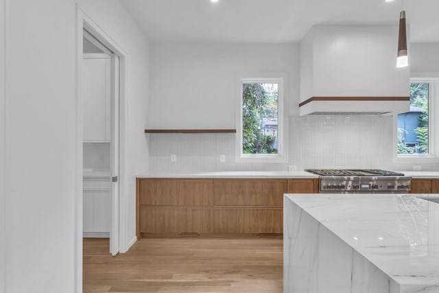 kitchen with custom exhaust hood, hanging light fixtures, light hardwood / wood-style flooring, light stone countertops, and stainless steel range