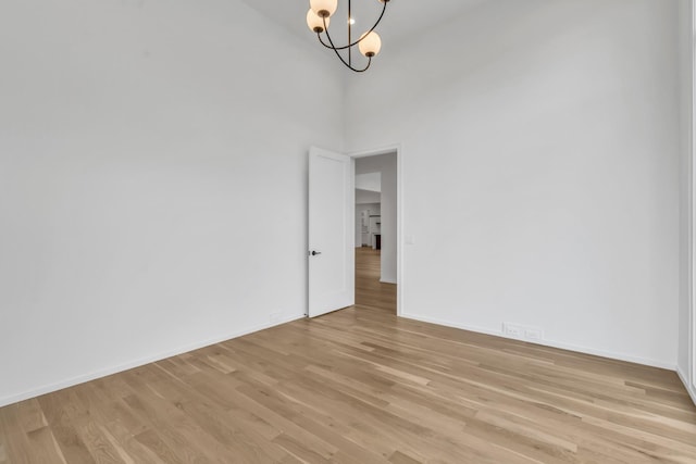 empty room with light hardwood / wood-style floors, a high ceiling, and an inviting chandelier