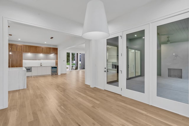 unfurnished living room with sink, a fireplace, beverage cooler, and light hardwood / wood-style flooring