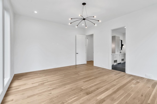 unfurnished room featuring light wood-type flooring, sink, and an inviting chandelier