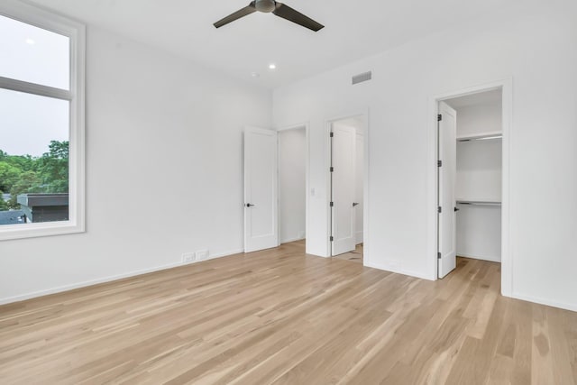 unfurnished bedroom with light wood-type flooring, a closet, a spacious closet, and ceiling fan