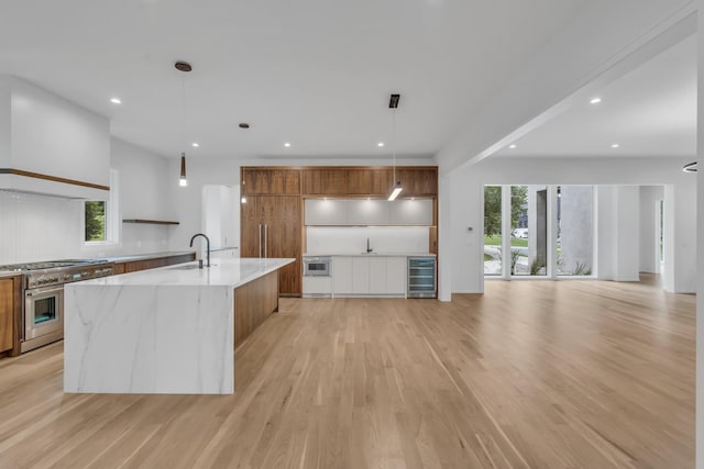 kitchen with sink, stainless steel appliances, wine cooler, pendant lighting, and light wood-type flooring