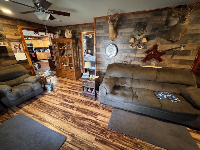 living room with hardwood / wood-style flooring, ceiling fan, and wooden walls