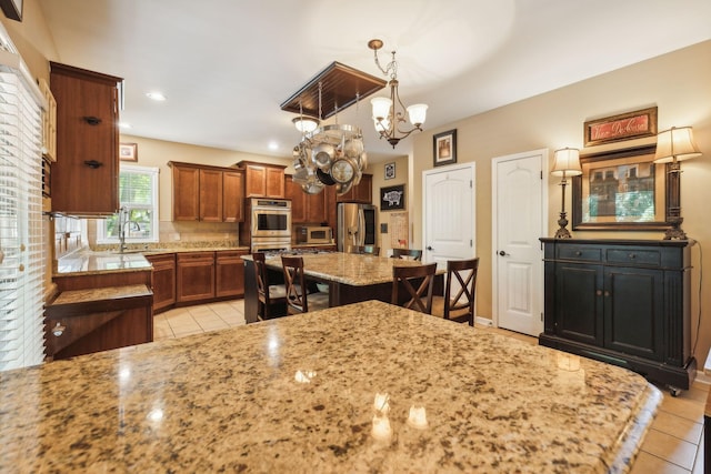 kitchen featuring light stone counters, a notable chandelier, decorative light fixtures, a kitchen island, and appliances with stainless steel finishes