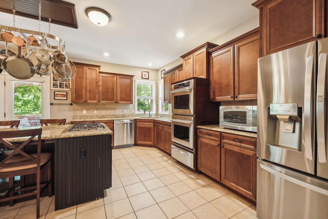 kitchen featuring light tile patterned floors, light stone countertops, stainless steel appliances, and a breakfast bar area