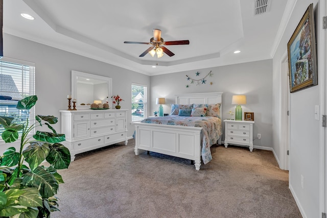 carpeted bedroom featuring a raised ceiling, multiple windows, crown molding, and ceiling fan