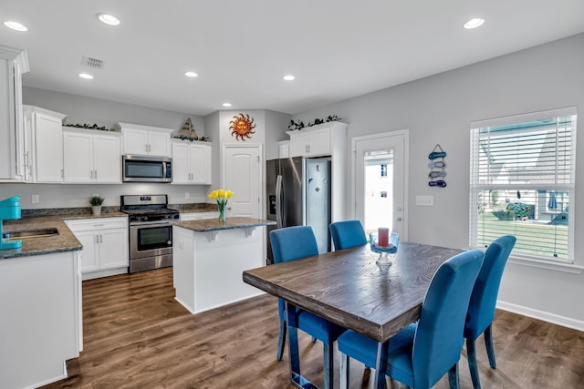 kitchen with appliances with stainless steel finishes, a center island, white cabinetry, and dark hardwood / wood-style flooring