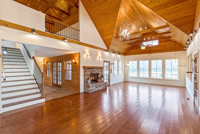 unfurnished living room featuring wooden ceiling, ceiling fan with notable chandelier, a stone fireplace, hardwood / wood-style flooring, and a towering ceiling