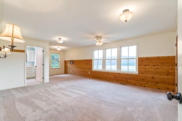 carpeted empty room featuring wood walls, crown molding, and ceiling fan