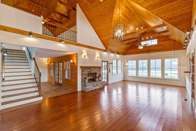 unfurnished living room featuring a towering ceiling, wood ceiling, ceiling fan with notable chandelier, hardwood / wood-style flooring, and a fireplace