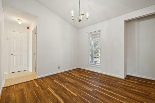 spare room featuring a notable chandelier, dark wood-type flooring, and vaulted ceiling