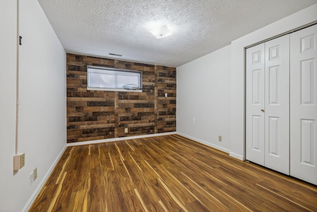 unfurnished bedroom featuring dark hardwood / wood-style floors, a textured ceiling, wooden walls, and a closet