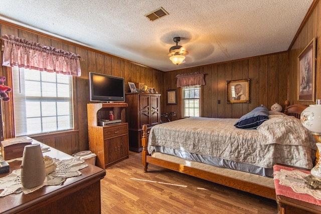 bedroom with a textured ceiling, ceiling fan, wood walls, and light wood-type flooring