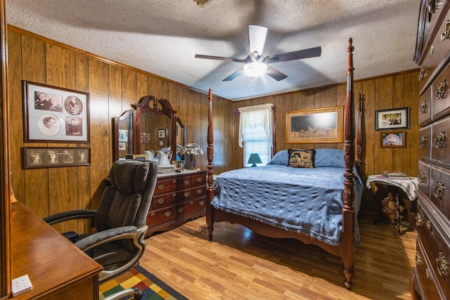 bedroom with a textured ceiling, light hardwood / wood-style flooring, ceiling fan, and wooden walls