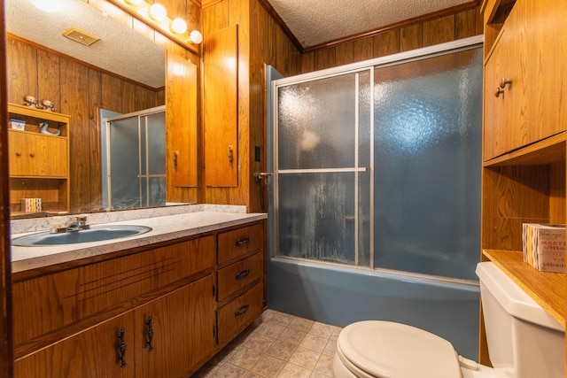 full bathroom with a textured ceiling, toilet, shower / bath combination with glass door, wooden walls, and vanity