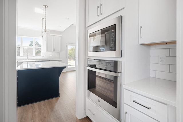 kitchen with light wood finished floors, white cabinetry, oven, and built in microwave