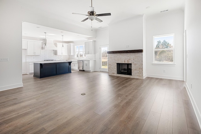 unfurnished living room featuring ceiling fan, a fireplace, wood finished floors, and baseboards