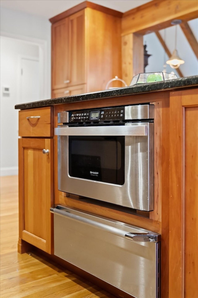 kitchen featuring light hardwood / wood-style flooring, dark stone countertops, and stainless steel oven