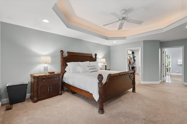 bedroom with light carpet, a raised ceiling, a walk in closet, ceiling fan, and a closet